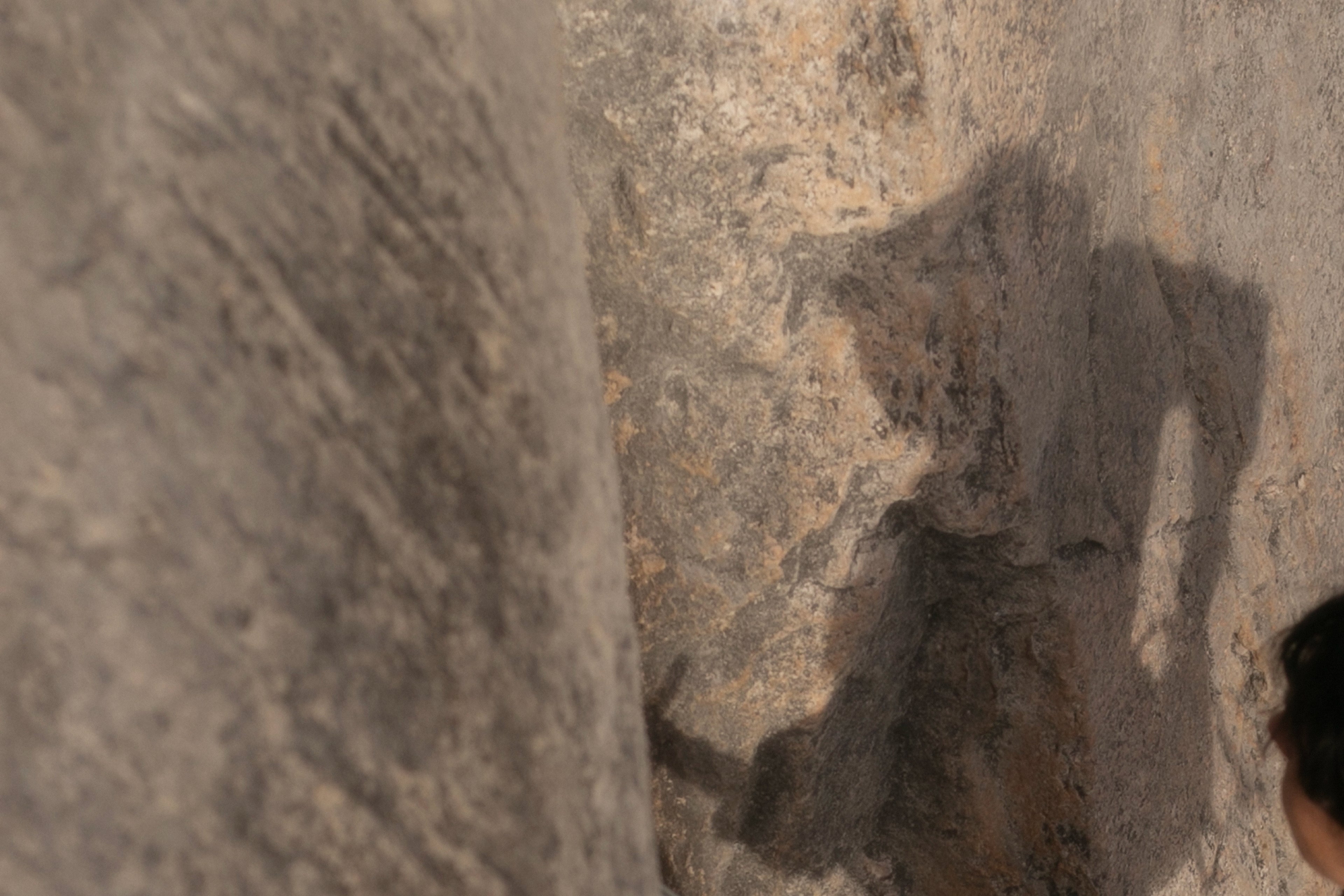 Sport climber climbing on outdoor crag and looking at their shadow on the rock.