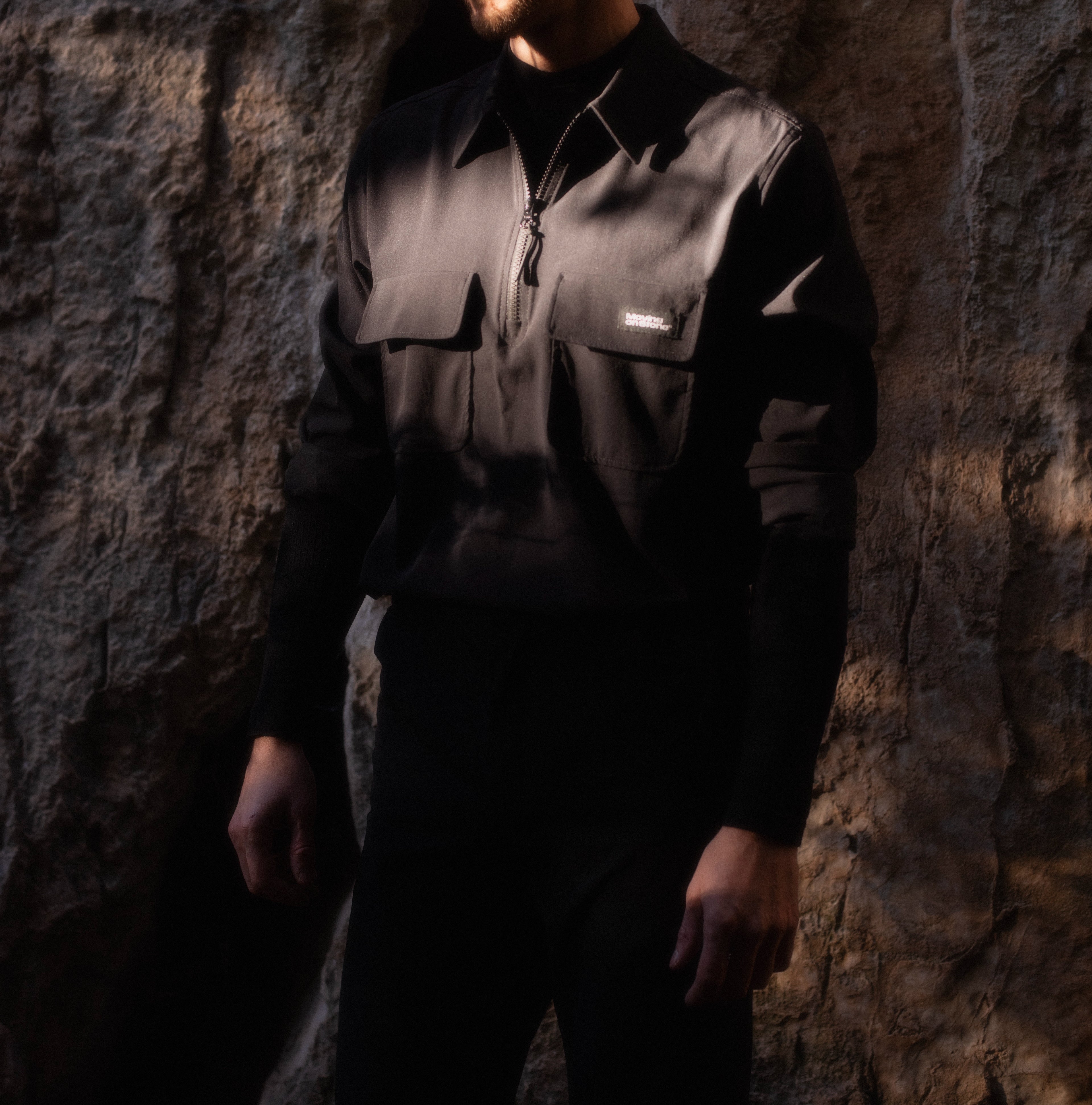 Sunlit climber standing in front of a rock face wearing a black lightweight performance climbing shirt.
