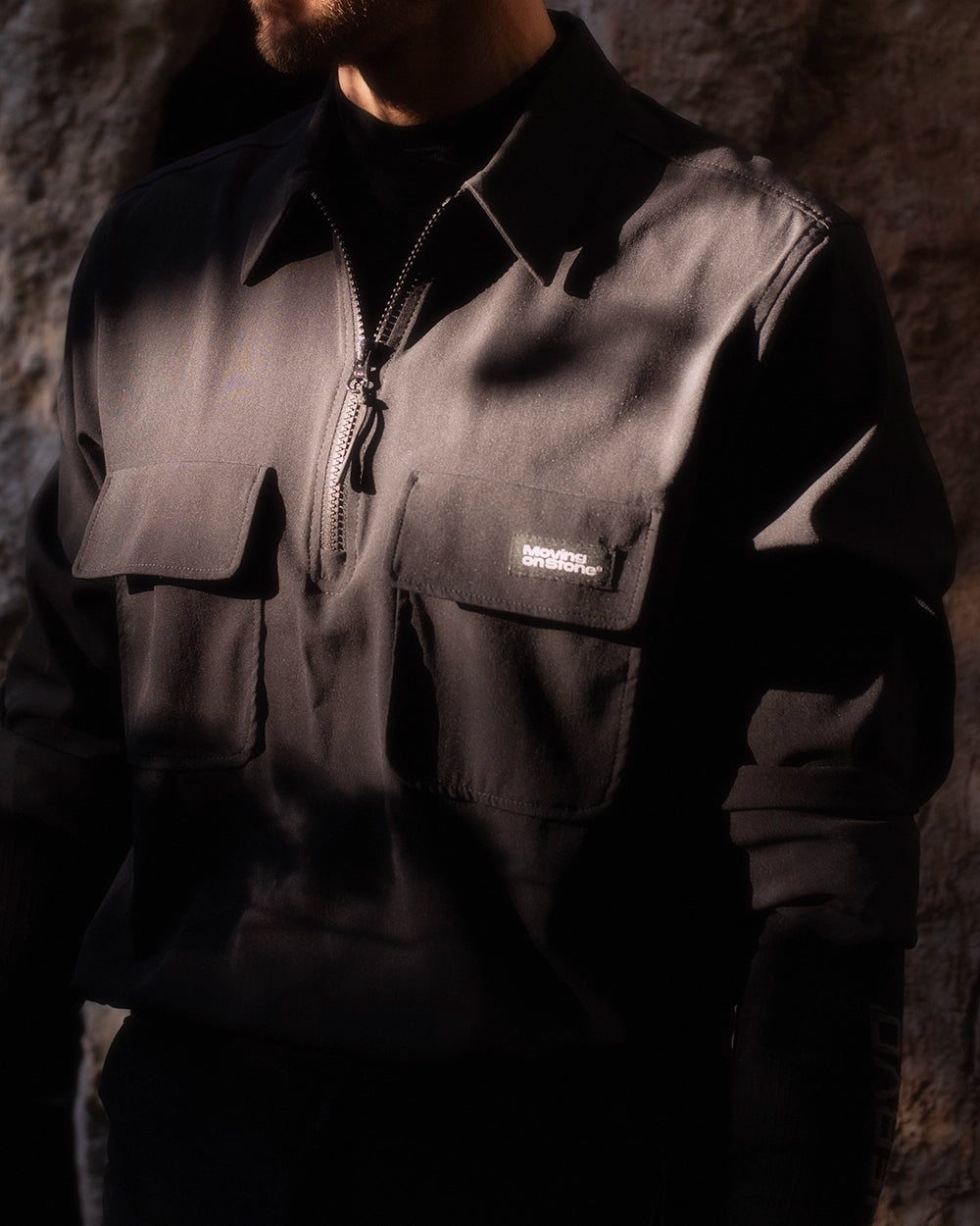 A climber standing in front of a rock face wearing a black lightweight performance climbing top.